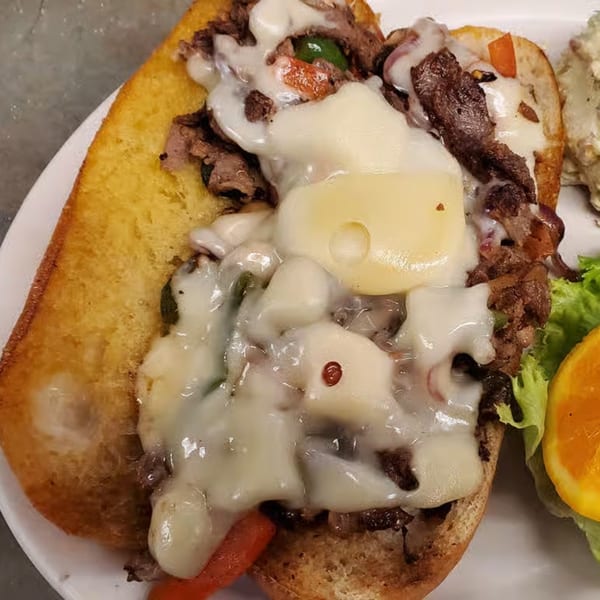 A close-up of a Philly cheesesteak sandwich from The Sandwich Company, overflowing with melted cheese.