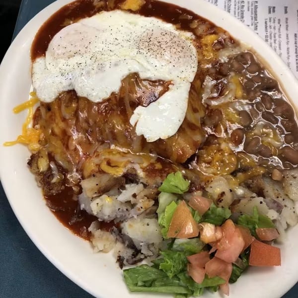 Hearty breakfast plate with two fried eggs, potatoes, beans, gravy, and a side salad.