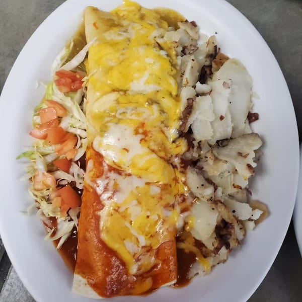A burrito covered in red and green sauce with melted cheese, served with a side of home fries.
