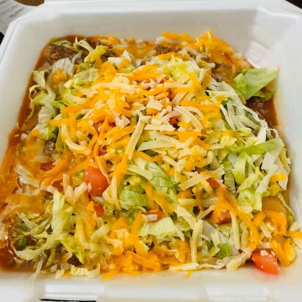A takeout container filled with a hearty dish topped with shredded lettuce, cheese, and diced tomatoes.