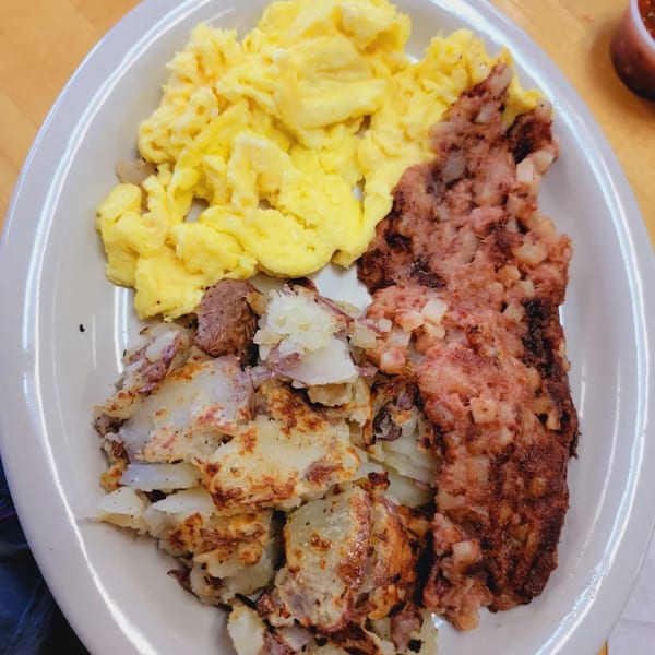 A breakfast plate with scrambled eggs, crispy home fries, and corned beef hash.