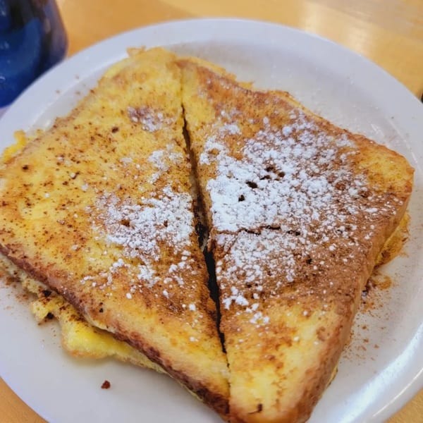 Two slices of French toast, dusted with powdered sugar and cinnamon, on a white plate.