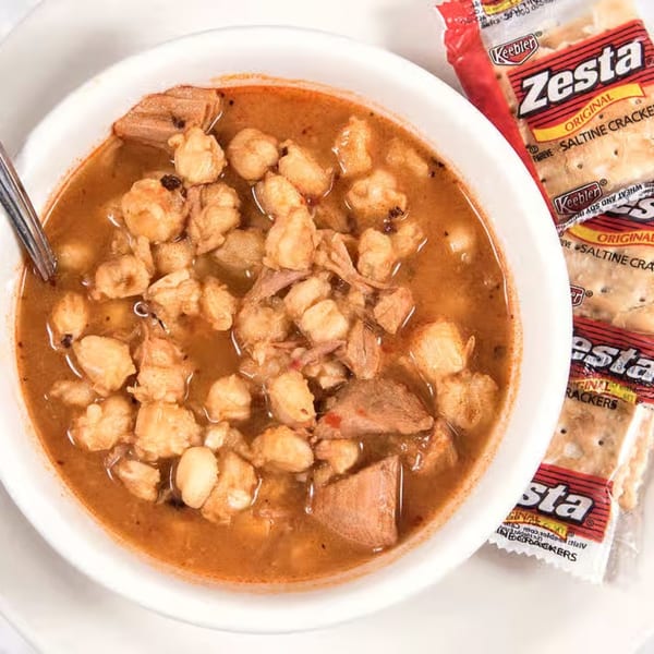 Hearty bowl of The Sandwich Company's pozole soup with pork and hominy, served with saltine crackers.